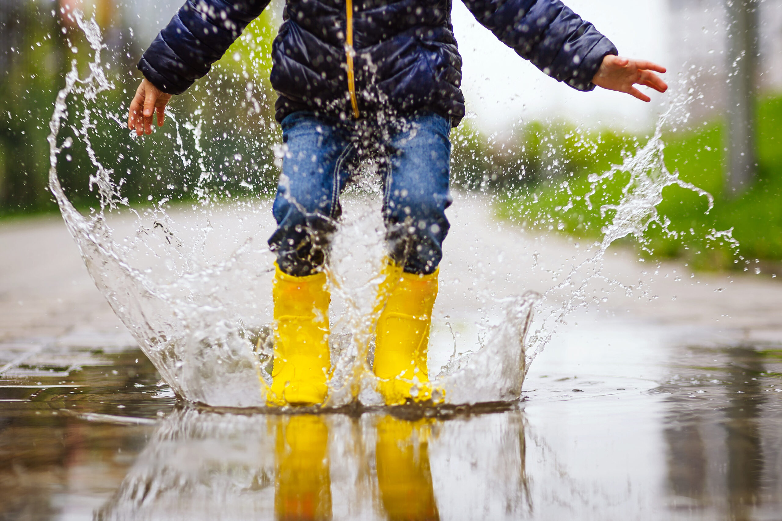 Närbild på barn som hoppar i vattenpöl iklädd gula gummistövlar under en promenad ute.
