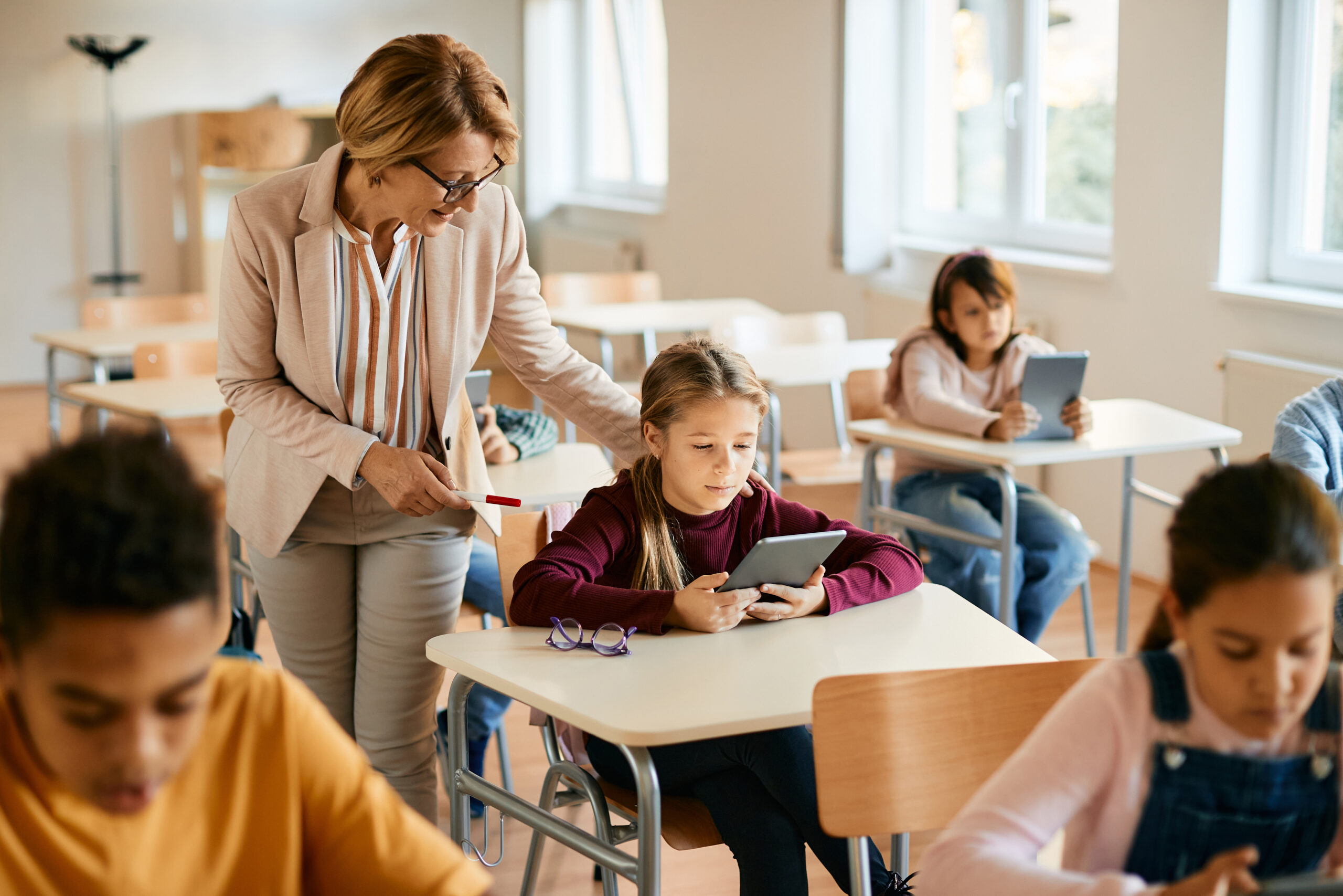 Lärare som hjälper ung grundskoleelev att använda en digital surfplatta som läromedel.