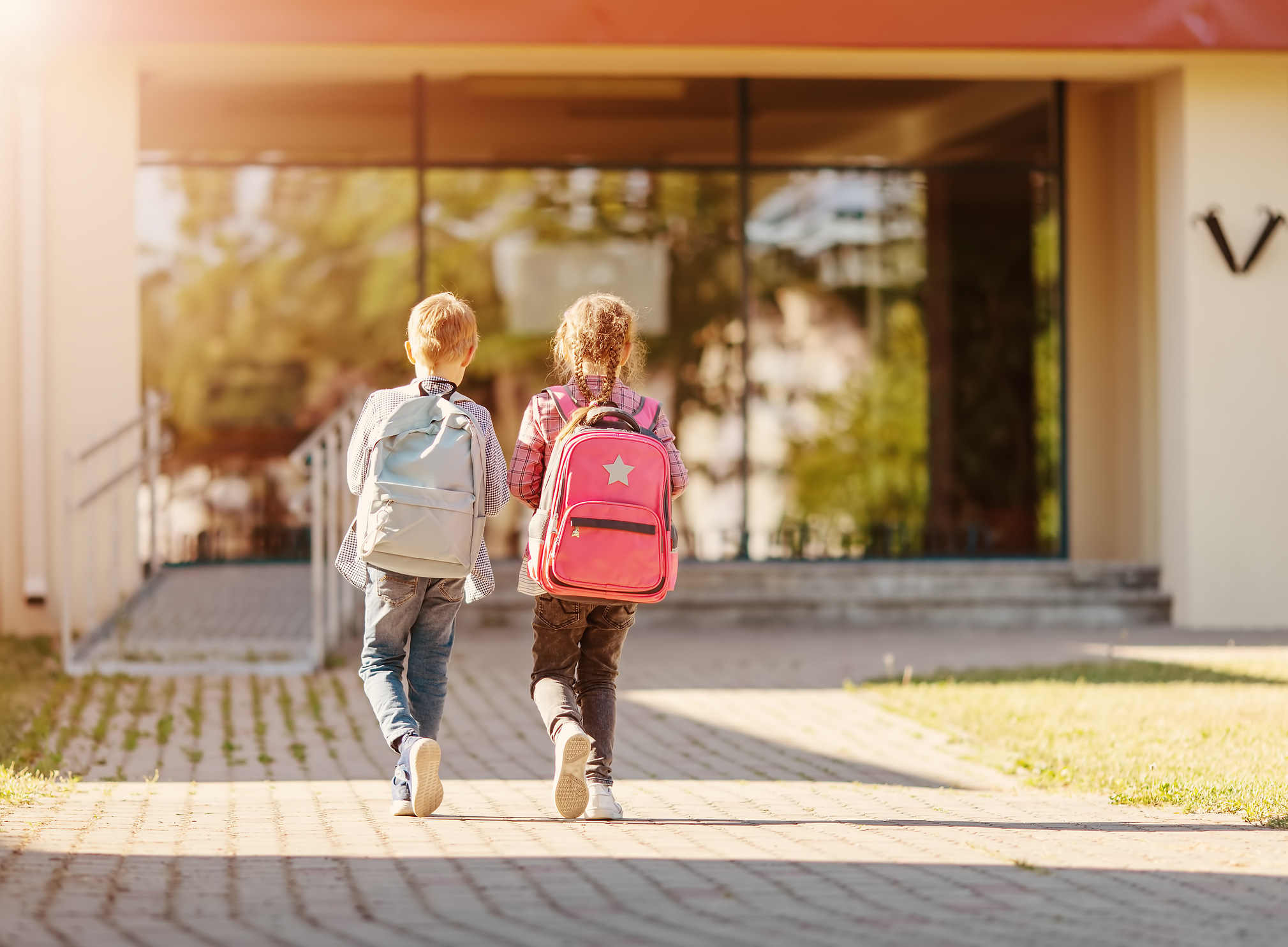 Flicka och pojke går tillsammans på skolgård mot en skola där de ska studera.